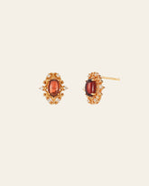 The Vivien Garnet Earrings by CAMELLIA are gold accessories with garnet-like oval red stones in ornate designs, accented with small clear stones. Hypoallergenic for all-day comfort, they are elegantly displayed on a light background.